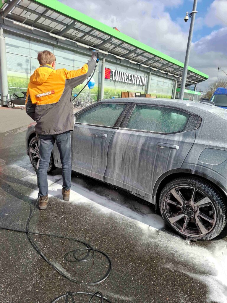 een auto wordt door personeelslid Hornbach voor de winkel gewassen met hogedrukspuit.